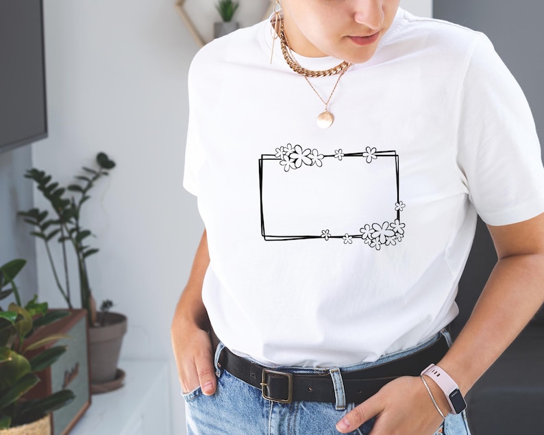 May include: White t-shirt with a black outline of a rectangle with flowers around it.