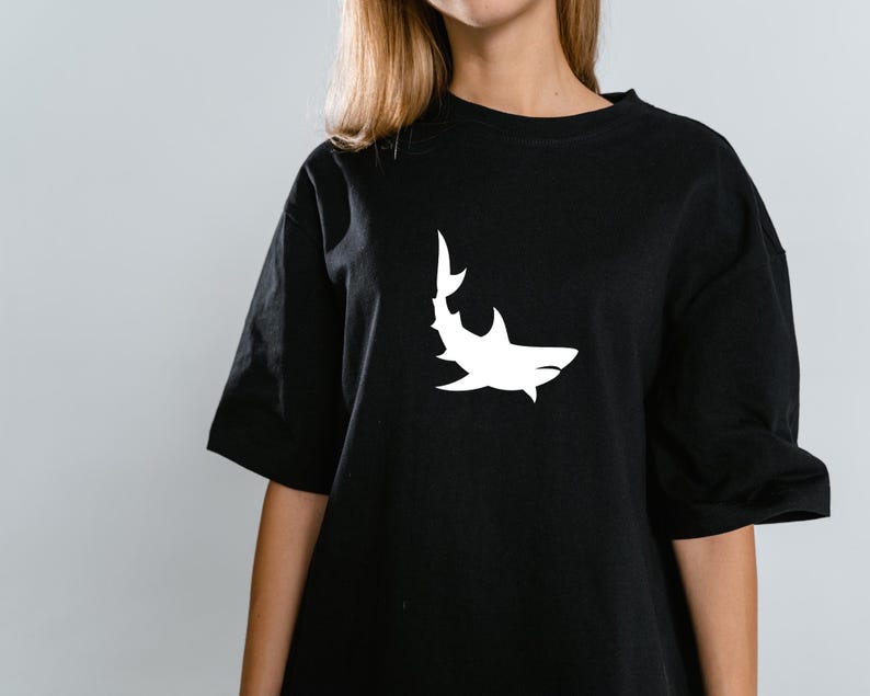 Puede incluir: Una camiseta negra con un gr&aacute;fico de silueta de tibur&oacute;n blanco.