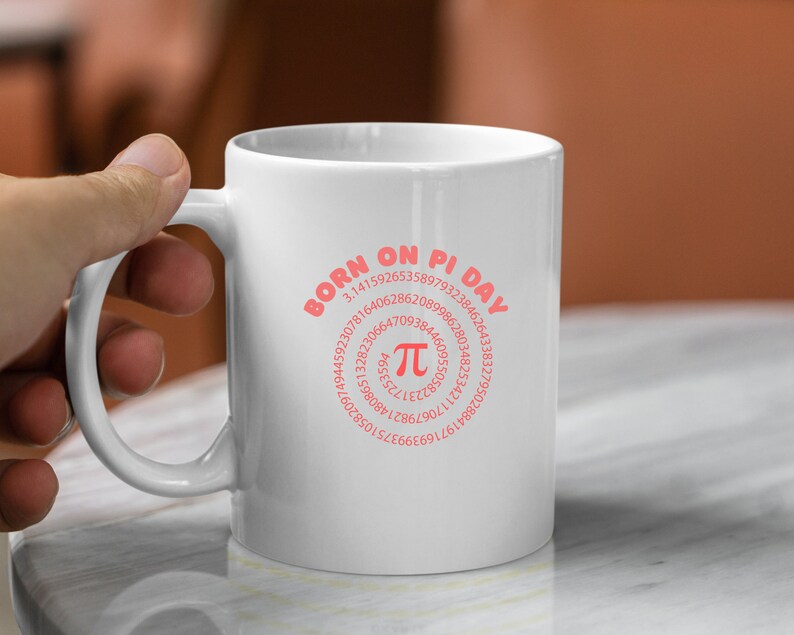 K&ouml;nnte beinhalten: Wei&szlig;e Keramiktasse mit einem rosafarbenen Design, auf dem "Geboren am Pi-Tag" steht und eine Spirale aus den Ziffern von Pi mit einem gro&szlig;en Pi-Symbol in der Mitte zu sehen ist.