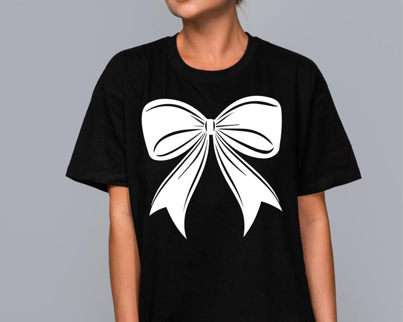 May include: Black t-shirt with a large white bow graphic printed on the front. The bow is a simple, elegant design. The t-shirt is a casual item of clothing.