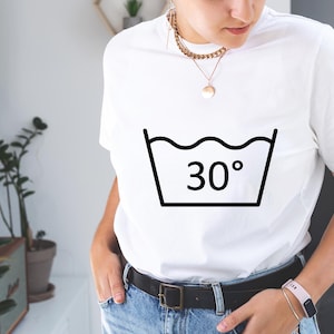 Może przedstawiać: Biała koszulka z czarnym symbolem pielęgnacji odzieży, na kt&oacute;rym widnieje napis "30&deg;".
