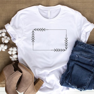 May include: White t-shirt with a black outline of a rectangle with leafy branches at each corner.