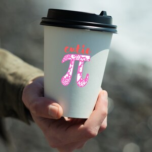K&ouml;nnte beinhalten: Ein wei&szlig;er To-Go-Becher mit schwarzem Deckel. Der Becher hat ein pinkfarbenes und wei&szlig;es Design mit dem mathematischen Symbol Pi und dem Wort "cutie" dar&uuml;ber.