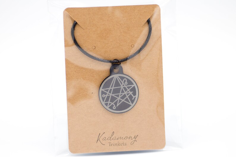May include: A black necklace with a silver pendant featuring a five-pointed star with intricate lines. The pendant is on a brown card with the text "Kadamony Trinkets".