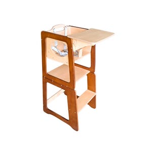 Pode incluir: Uma torre de aprendizagem de madeira para crianças pequenas com acabamento natural. A torre tem vários níveis, incluindo uma plataforma e uma pequena mesa. Possui cintas de segurança e foi projetada para ajudar as crianças a alcançar bancadas.