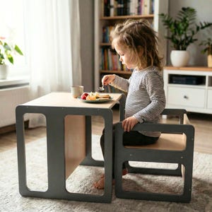 May include: A child-sized table and chair set. The table and chair have a gray frame with a natural wood-tone tabletop and seat. The child is eating fruit from a plate on the table. The set is designed for children's activities and meal times.