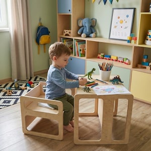 Op de afbeelding: Een houten tafel- en stoelset voor kinderen. De lichtgekleurde houten meubels hebben een eenvoudig, modern design. Het kind tekent met kleurpotloden op een stuk papier. Speelgoeddinosaurussen en een potloodhouder staan op de tafel.
