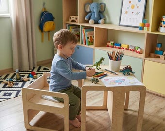 May include: A child's wooden table and chair set. The light-colored wood furniture has a simple, modern design. The child is drawing with crayons on a piece of paper. Toy dinosaurs and a pencil holder are on the table. A bookshelf is in the background.
