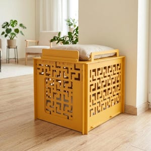May include: A mustard yellow pet crate with a geometric cut-out design. The crate has a flat top with a beige cushion. The crate is made of wood and is placed in a well-lit room with hardwood floors.