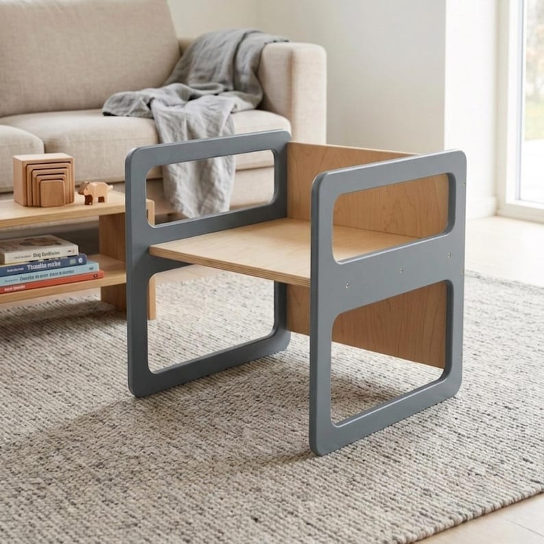 May include: A gray and natural wood children's chair with a rectangular frame and a seat. The chair has a modern design with rounded corners and a sturdy construction. The chair is designed for young children and is suitable for use in a playroom or nursery.