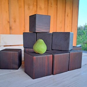 Könnte beinhalten: Ein Stapel dunkelbrauner Holzblöcke mit einer grünen Birne oben drauf. Die Blöcke sind in Pyramidenform angeordnet.