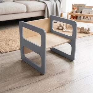 May include: A small, gray wooden chair with a natural wood seat and back. The chair has a simple, modern design with rounded edges and cut-out handles. The chair is approximately 12 inches wide, 12 inches deep, and 18 inches tall.
