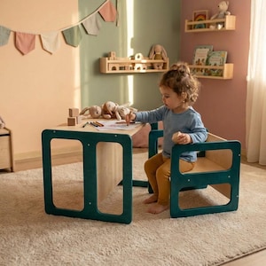 May include: A child's wooden table and chair set with a teal frame and natural wood tabletop and seat. The child is drawing on paper with colored pencils. The room has a neutral color palette with decorative shelves and a banner.