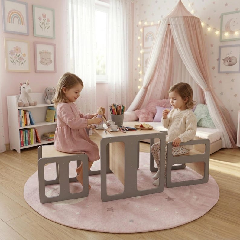 May include: A children's play table and two matching chairs in a light wood and gray color scheme. The table has a rectangular top and a gray frame. The chairs are small, square, and gray. The scene is set in a child's bedroom.