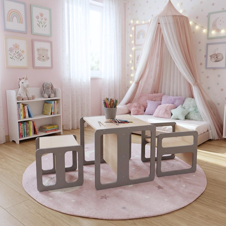 May include: A children's bedroom scene featuring a small table and two chairs with gray frames and light wood tops. A matching bookshelf and a round pink rug with star patterns are also present. The room is decorated with framed art and a canopy bed.