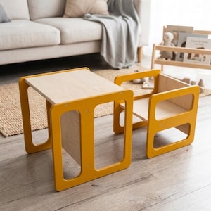 May include: A child's table and chair set. The table and chair have a mustard yellow frame with a natural wood tabletop and seat. The chair has a rectangular back and armrests. The set is made of wood and is designed for children.