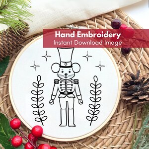 May include: Black and white line art embroidery pattern of a mouse dressed as a nutcracker soldier. The mouse is standing between two sprigs of leaves. The pattern is on a white background and is ready to be stitched.