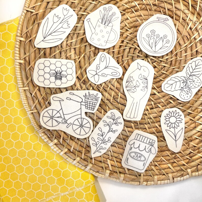 May include: A collection of eleven white stickers with black line art illustrations including a bee on a honeycomb, a bicycle with a flower basket, a bird, a jar labeled JAM, a sunflower, strawberries, a butterfly, and various floral designs.