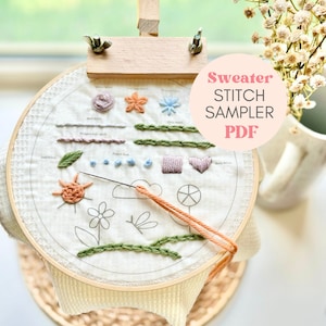 May include: A close-up of a white embroidery hoop with various stitches and designs, including a sun, a flower, a cloud, and leaves. The hoop is on a wooden stand and the text "Sweater Stitch Sampler PDF" is visible in a pink circle.
