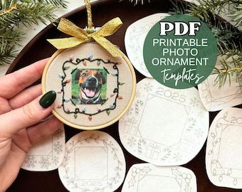 Könnte beinhalten: Ein runder Stickrahmen-Weihnachtsschmuck mit beigem Stoff, einem Foto eines Hundes, das von gestickten Lichterketten umrahmt ist, und einer goldenen Schleife. Mehrere weiße Papiervorlagen mit aufgedruckten weihnachtlichen Motiven liegen bei.