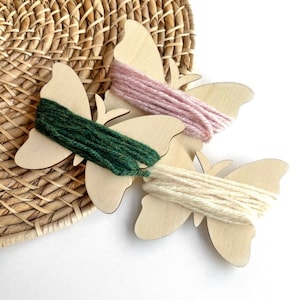 May include: Three wooden butterfly shapes with yarn wound around them. The butterflies are in shades of pink, green, and cream.