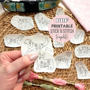 May include: A collection of printable stick and stitch templates featuring dog illustrations with floral accents. The templates are displayed with embroidery floss, a dog collar, and a pink fabric square. The text "PDF Printable Stick & Stitch Template" is visible.
