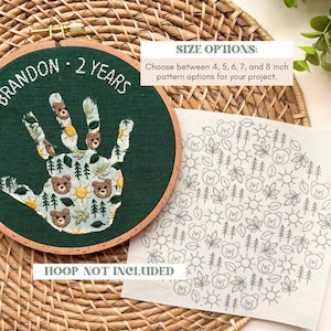 May include: An embroidery hoop with a green fabric featuring a handprint design with bears, trees, and suns. The text "BRANDON - 2 YEARS" is embroidered above the handprint. A separate fabric piece shows a pattern of bears, trees, leaves, and suns. The text "HOOP NOT INCLUDED" is visible.