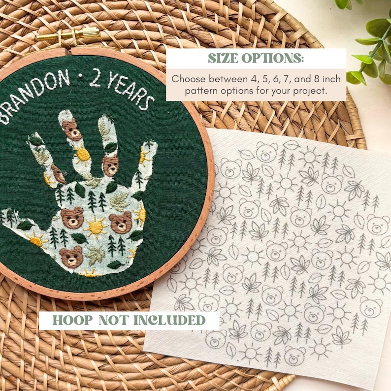 May include: An embroidery hoop with a green fabric featuring a handprint design with bears, trees, and suns. The text "BRANDON - 2 YEARS" is embroidered above the handprint. A separate fabric piece shows a pattern of bears, trees, leaves, and suns. The text "HOOP NOT INCLUDED" is visible.