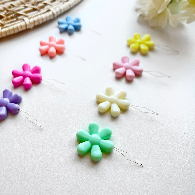 May include: A set of eight colorful flower-shaped threaders with metal needles. The threaders are in various pastel colors, including pink, purple, light blue, yellow, and green.
