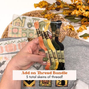 May include: A bundle of five embroidery thread skeins in orange, light green, yellow, dark green, and black, packaged in clear plastic. The skeins feature labels with the text DMC 25 and specific color codes, held together for cross-stitch projects.