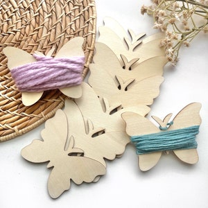 May include: Wooden butterfly shapes with holes for stringing yarn. Two butterflies have pink and teal yarn wound around them.