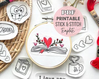 May include: A round wooden embroidery hoop containing white fabric with a stitched open book and red heart design, surrounded by various stick and stitch templates featuring books, hearts, and the text I love you, with red embroidery floss.