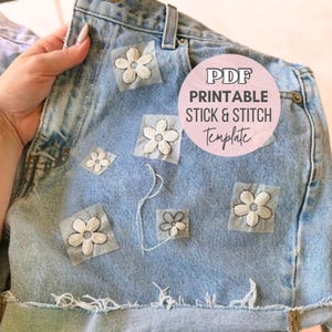 Könnte beinhalten: Hellblaue Jeansshorts mit gestickten weißen Blumenaufnähern. Die Shorts haben einen Used-Look mit ausgefransten Kanten. Ein rosa Kreis-Grafik liest sich "PDF Printable Stick & Stitch Template".