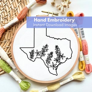 May include: A black and white line drawing of the state of Texas with bluebonnets inside the outline. The drawing is on a white fabric stretched over a wooden embroidery hoop. The hoop is surrounded by colorful embroidery floss.