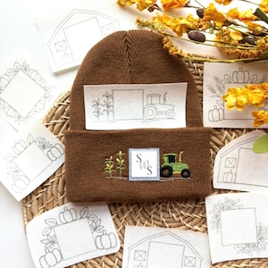 May include: A brown knit beanie featuring a rectangular patch with an embroidered green tractor, corn stalks, and a square label with the letters S and W. A rectangular fabric piece with a line drawing of a tractor and corn is placed above.
