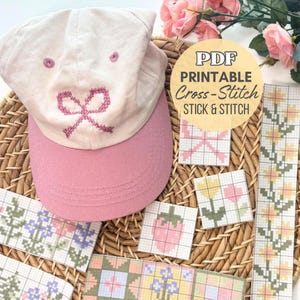 May include: A light pink baseball cap with a pink embroidered bow design. The cap is next to several cross-stitch patterns, including a bow, flowers, and a strawberry. The image also includes a PDF printable cross-stitch sticker.
