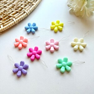 May include: Assortment of colorful plastic flower-shaped threaders with metal needles. The threaders are in shades of pink, blue, yellow, green, and white.