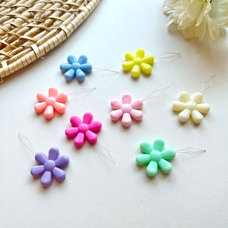 May include: Assortment of colorful plastic flower-shaped threaders with metal needles. The threaders are in shades of pink, blue, yellow, green, and white.