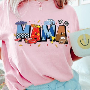 May include: Pink t-shirt with a graphic of the word "MAMA" in colorful letters with cartoon cars from the movie Cars.
