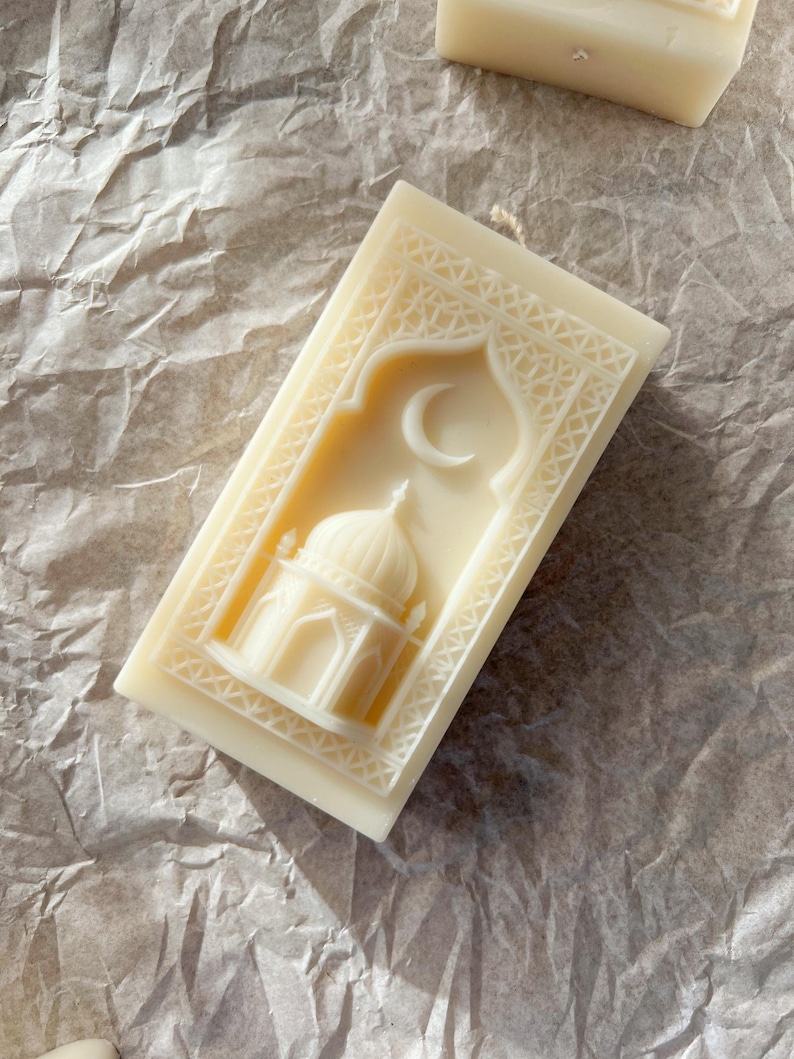 K&ouml;nnte beinhalten: Elfenbeinfarbene rechteckige Kerze mit detailliertem Reliefdesign. Das Design zeigt eine Moschee mit Kuppel und Mondsichel, umrahmt von einem verzierten Rand. Die Kerze ist unparf&uuml;miert und hat ein nat&uuml;rliches, handgemachtes Aussehen.