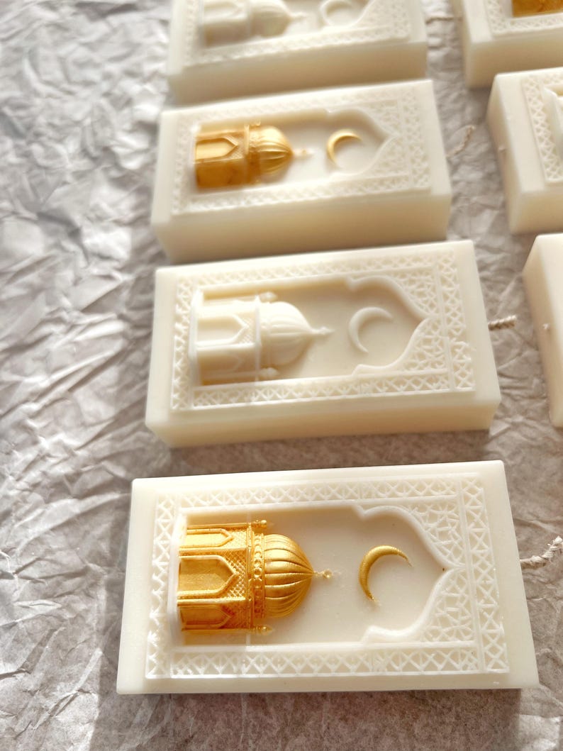 K&ouml;nnte beinhalten: Elfenbeinfarbene rechteckige Kerzen mit goldenen Moschee- und Mondsichel-Designs. Die Kerzen haben komplizierte, gepr&auml;gte Muster an den R&auml;ndern. Die Moscheedome sind goldfarben bemalt, und die Halbmonde sind ebenfalls goldfarben.