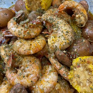 May include: A close-up of a bowl of seafood boil with shrimp, corn on the cob, potatoes, and sausage. The shrimp are seasoned with herbs and spices and the corn is yellow with kernels.