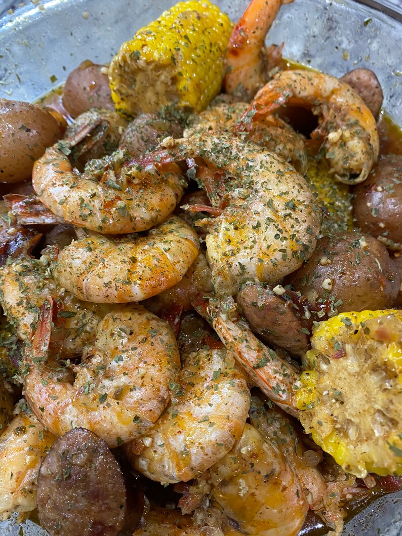 May include: A close-up of a bowl of seafood boil with shrimp, corn on the cob, potatoes, and sausage. The shrimp are seasoned with herbs and spices and the corn is yellow with kernels.