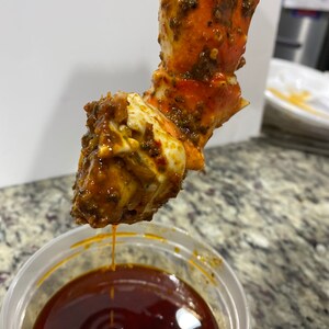 May include: A close-up of a crab leg dipped in a red sauce. The crab leg is covered in a brown and green seasoning.