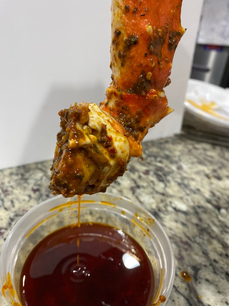 May include: A close-up of a crab leg dipped in a red sauce. The crab leg is covered in a brown and green seasoning.