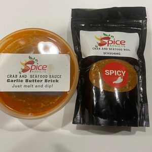 May include: Two containers of crab and seafood seasoning. One is a red sauce in a clear plastic container with a label that reads "Spice Addicts Crab and Seafood Sauce Garlic Butter Brick Just melt and dip!" The other is a black bag with a label that reads "Spice Addicts Crab and Seafood Boil Seasoning" with a red circle that says "Spicy" and a red chili pepper.