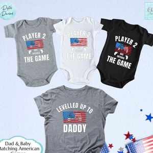 Puede incluir: Camisas a juego para padre y bebé con un diseño de bandera estadounidense. Las camisas para bebé dicen "Player 2 Has Entered The Game" y la camisa para adulto dice "Levelled Up To Daddy".