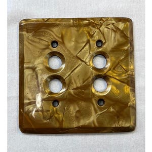 Peut inclure: Plaque de commutateur carrée vintage avec une finition marbrée brun doré. Le couvercle comporte six ouvertures circulaires pour les interrupteurs et quatre trous de vis. La surface présente un motif texturé et tourbillonnant.