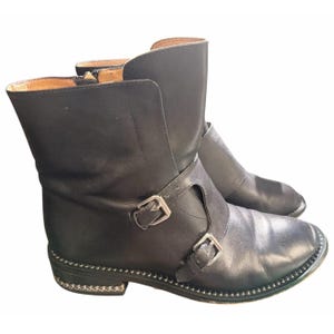 May include: A pair of black leather ankle boots with silver-tone buckles and a studded trim around the soles. The boots have a low heel and a rounded toe.