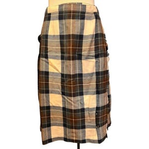May include: A knee-length plaid skirt in a neutral color palette of beige, brown, and navy blue. The skirt features a classic tartan pattern and a fringed edge detail. The skirt is made of a woven fabric.